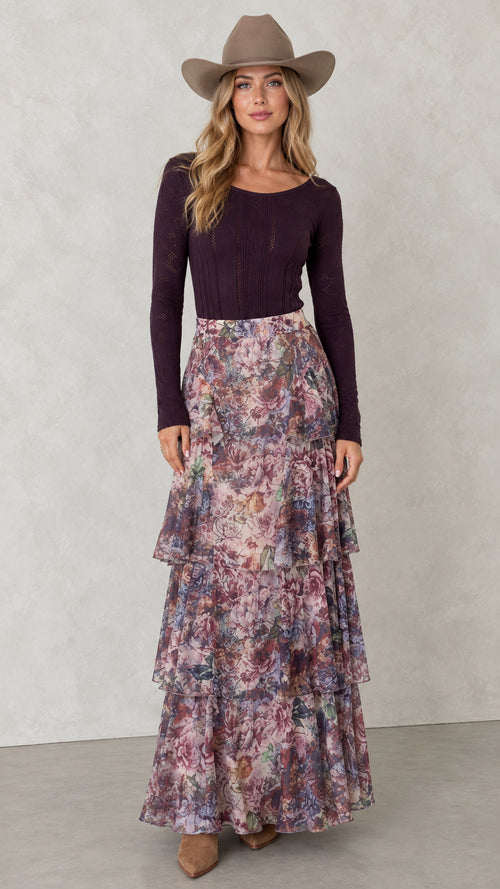 Front view of woman wearing Mauve Plum tiered floral maxi skirt with plum long sleeve top and hat