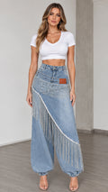 Front view of woman wearing light blue rhinestone fringe denim balloon pants with white crop top