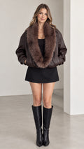 Front view of model wearing dark brown faux leather bomber jacket with plush fur collar